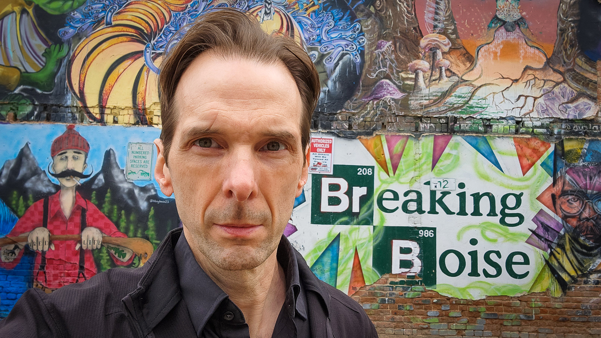 Motivational speaker Larry Weaver posing seriously in front of the Breaking Boise mural at Freak Alley Gallery in Boise, Idaho