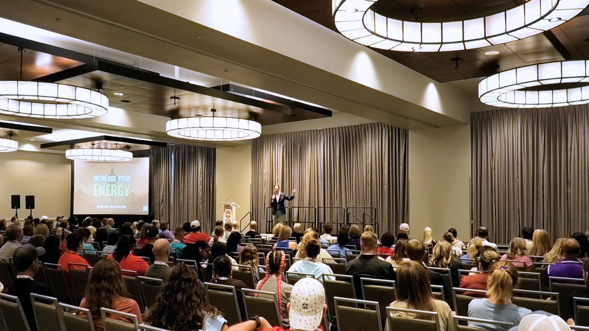 Larry Weaver speaking onstage for health and physical education professionals during a summer conference at Embassy Suites by Hilton Denton Convention Center in Denton, Texas.
