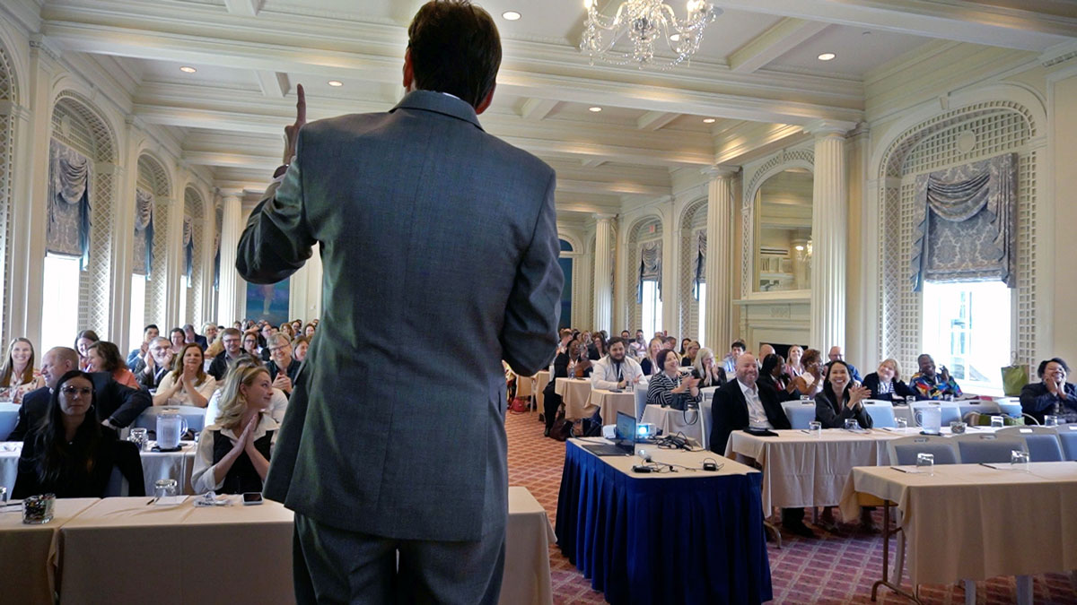 Larry Weaver speaking onstage for rehabilitation organization financial managers during an annual conference at The Otesaga Resort Hotel in Cooperstown, New York.