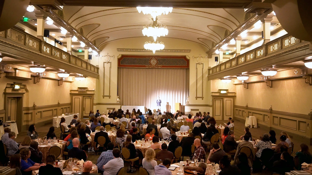 Larry Weaver speaking onstage for workers’ compensation agency staff during an appreciation luncheon at Hotel John Marshall in Richmond, Virginia.